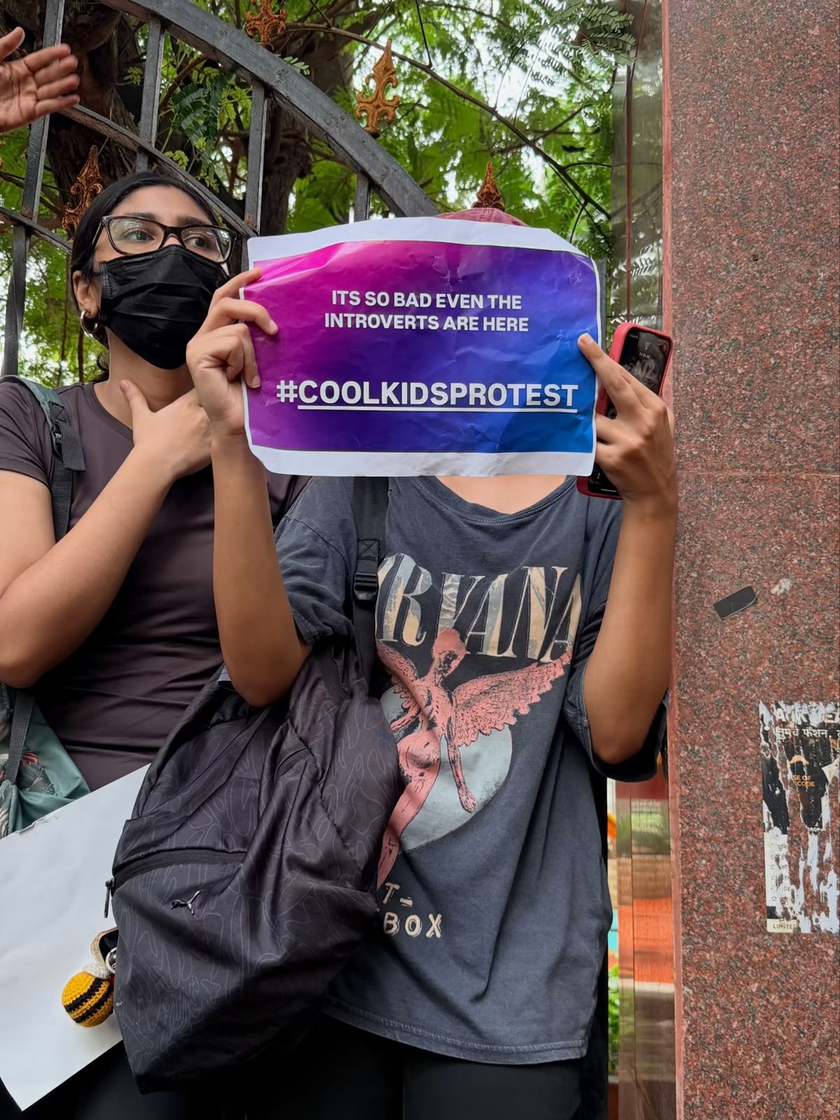 A protester holds a printed sign reading 'It's so bad even the introverts are here — #coolkidsprotest'