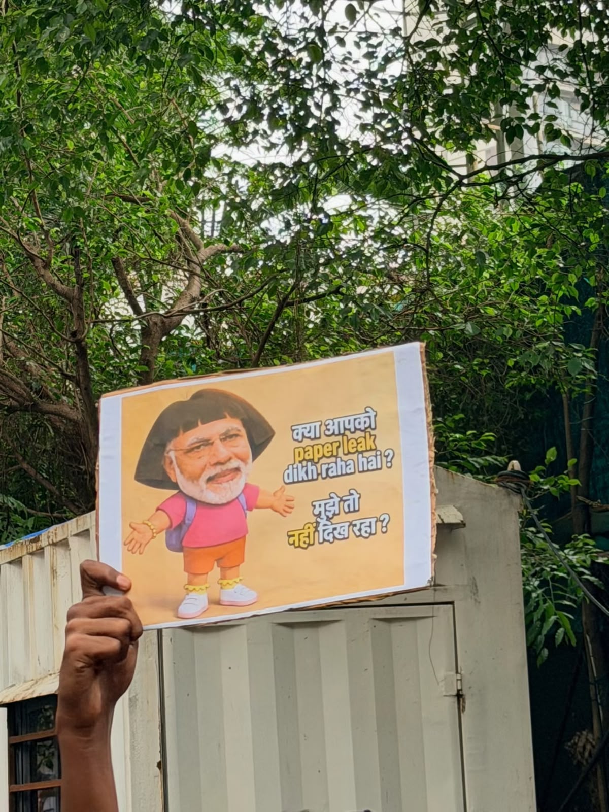 A raised fist holds a hand-made satirical placard above a street