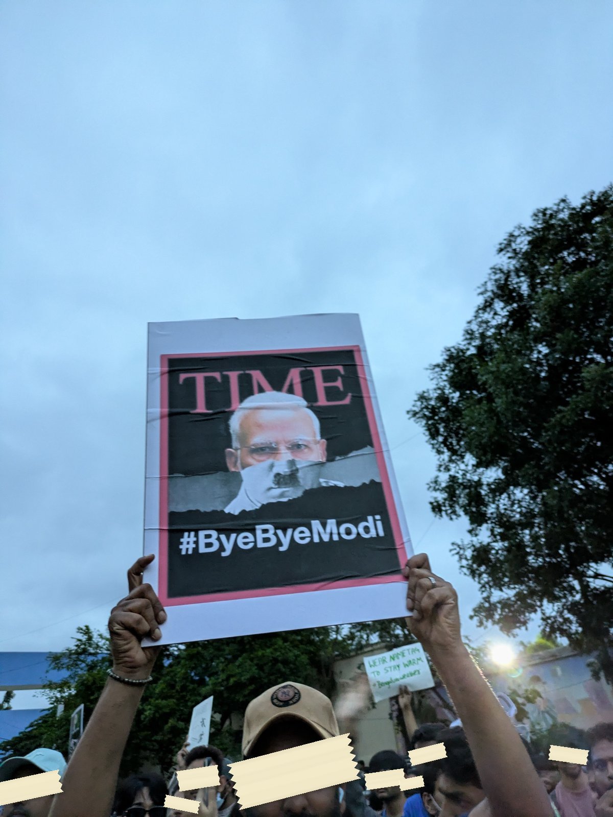 A print styled as a TIME magazine cover with the hashtag ByeByeModi held above the crowd