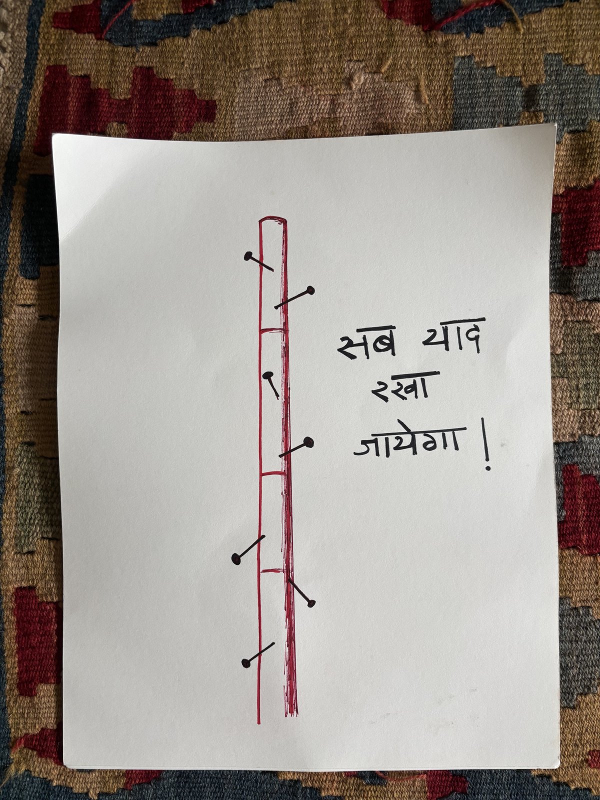 A drawing on white paper of a lathi studded with nails, captioned in Hindi that everything will be remembered