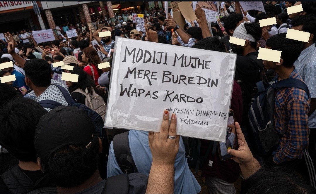 A hand-lettered sign in a dense crowd reads Modiji mujhe mere bure din wapas kardo, hashtag Resign Dharmendra Pradhan
