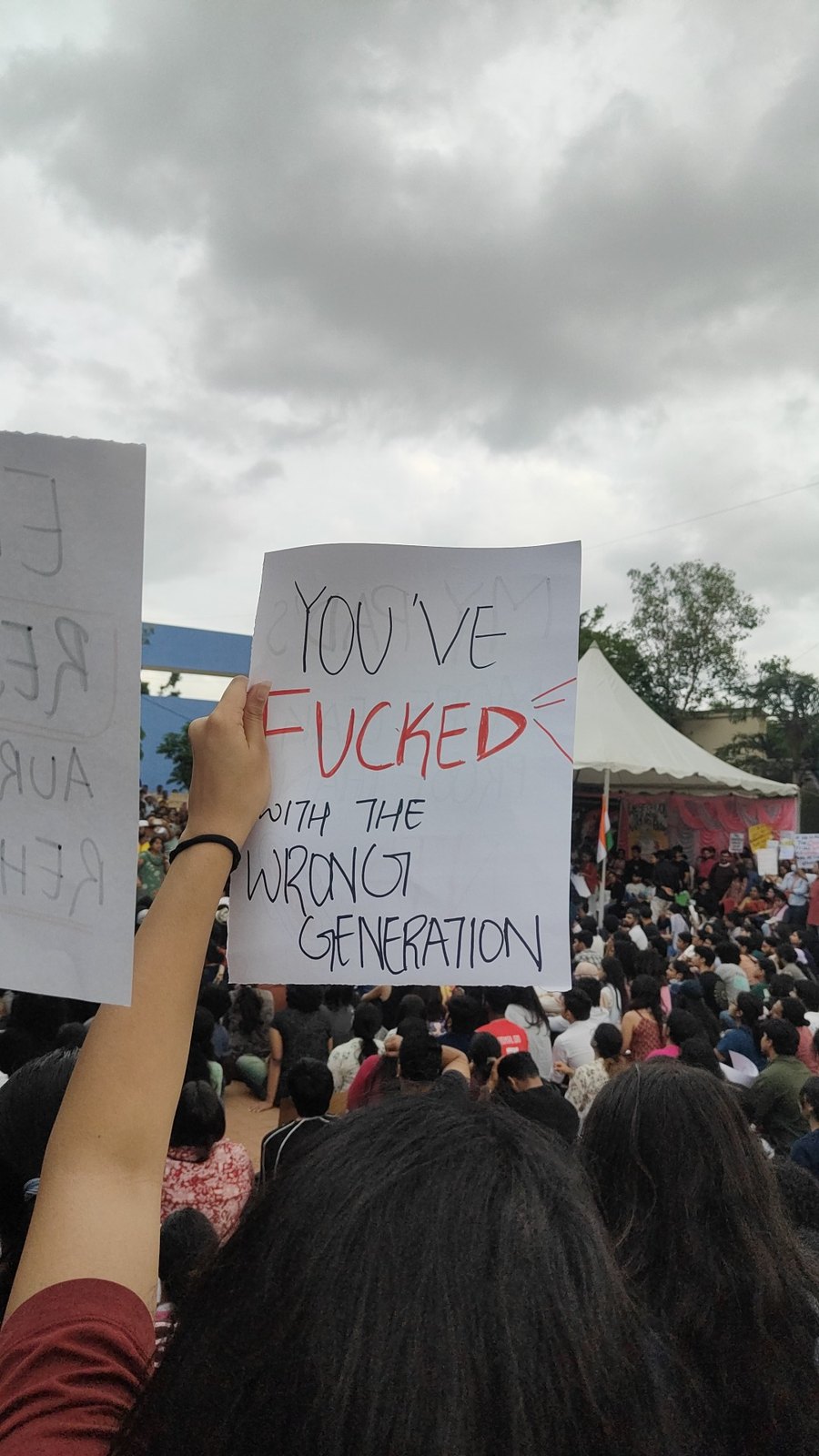 A raised hand holds a sheet reading You've fucked with the wrong generation above a seated crowd under a grey sky