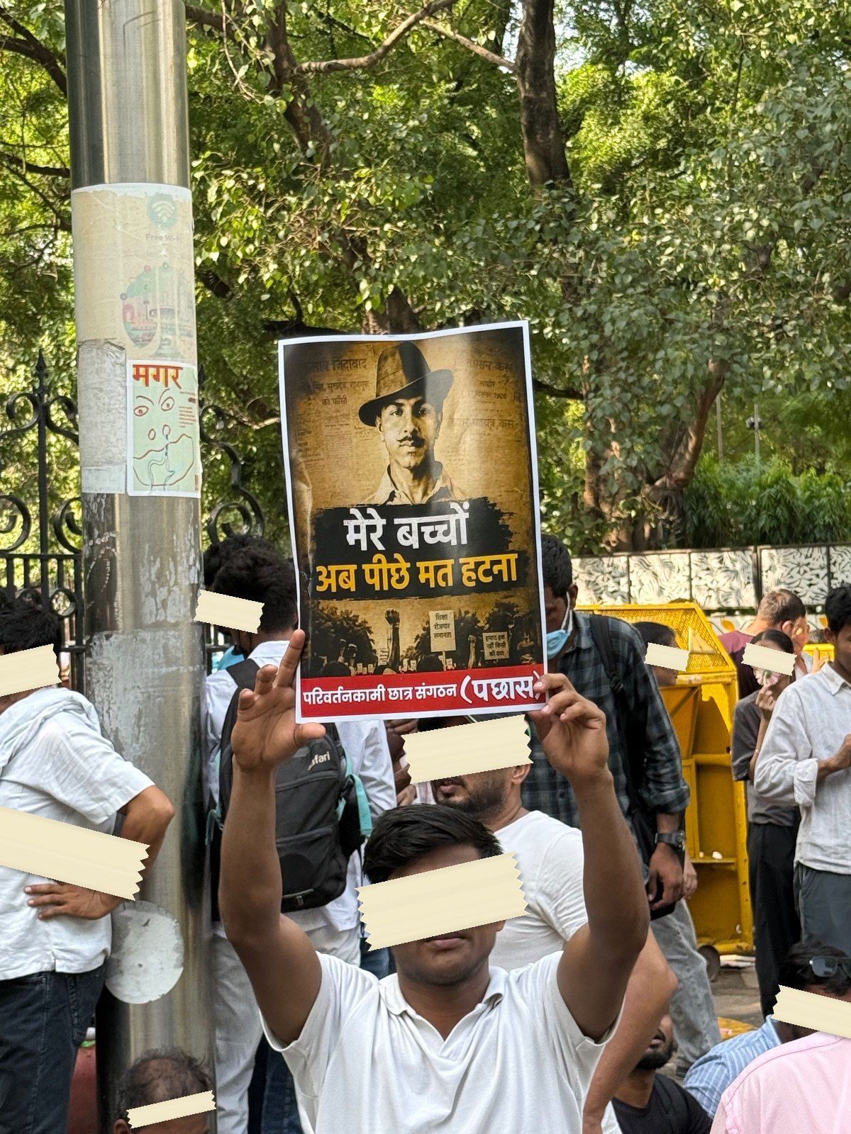 A printed poster of Bhagat Singh held above a crowd at Jantar Mantar, captioned in Hindi