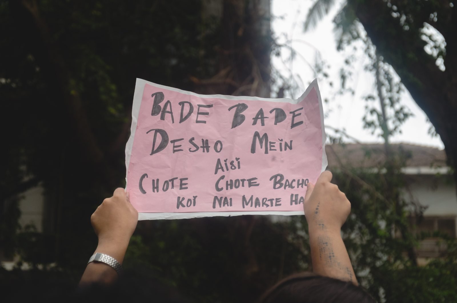 A pink sheet of paper held against the sky, hand-lettered in Roman-script Hindi