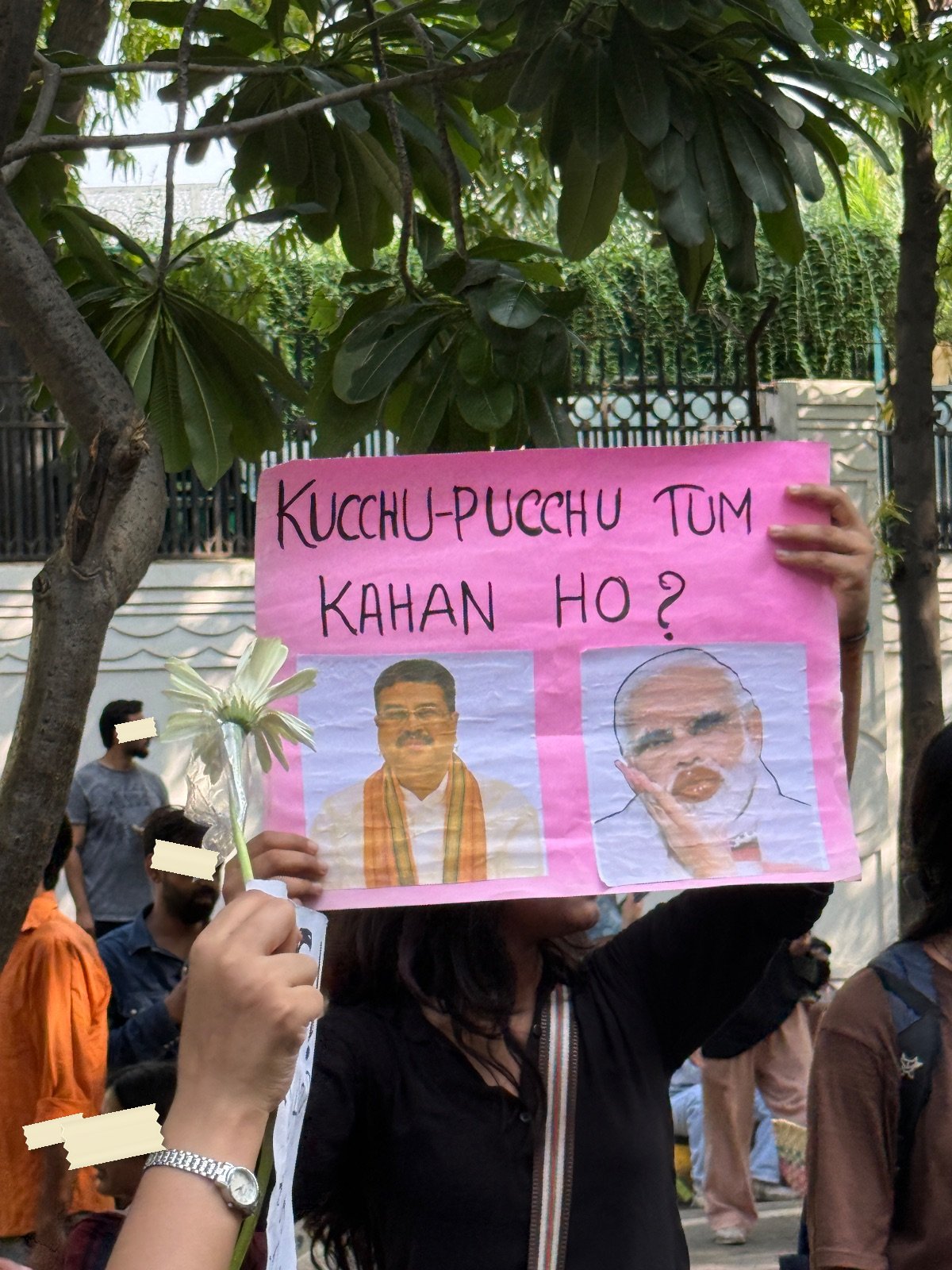 A pink placard reading Kucchu-Pucchu tum kahan ho, with a photograph of the education minister and a caricature of the Prime Minister blowing a kiss