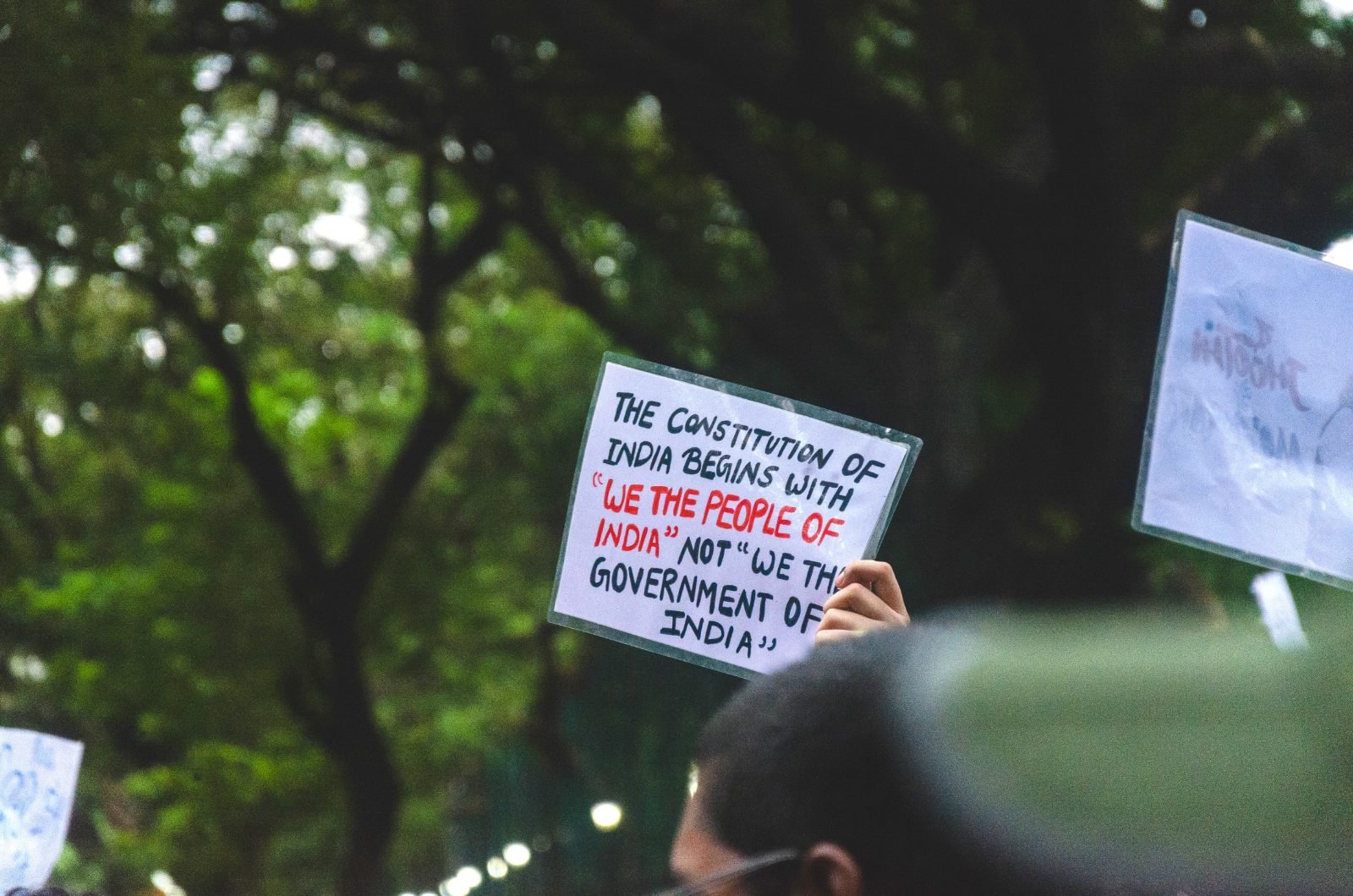 A small hand-lettered placard reading The Constitution of India begins with We The People Of India, not We The Government Of India