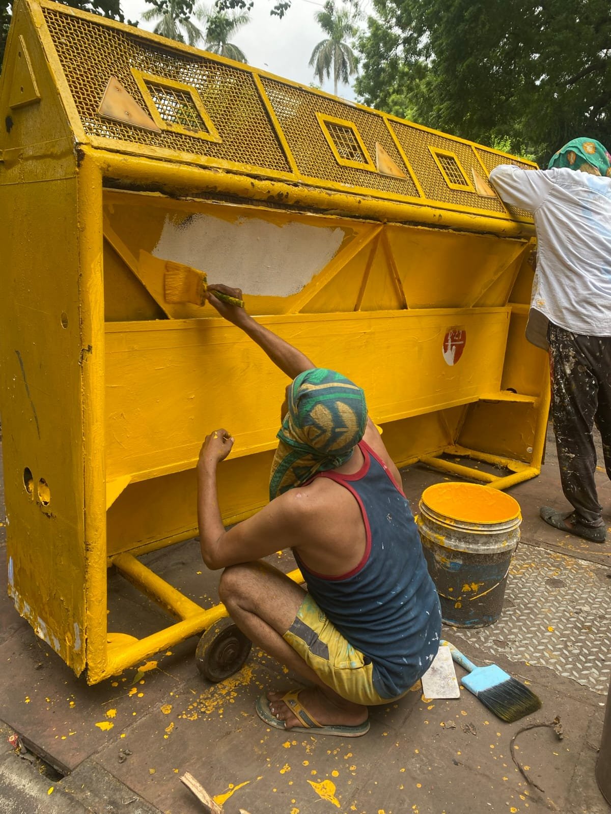 A worker crouched beside a police barricade, painting it back to plain yellow