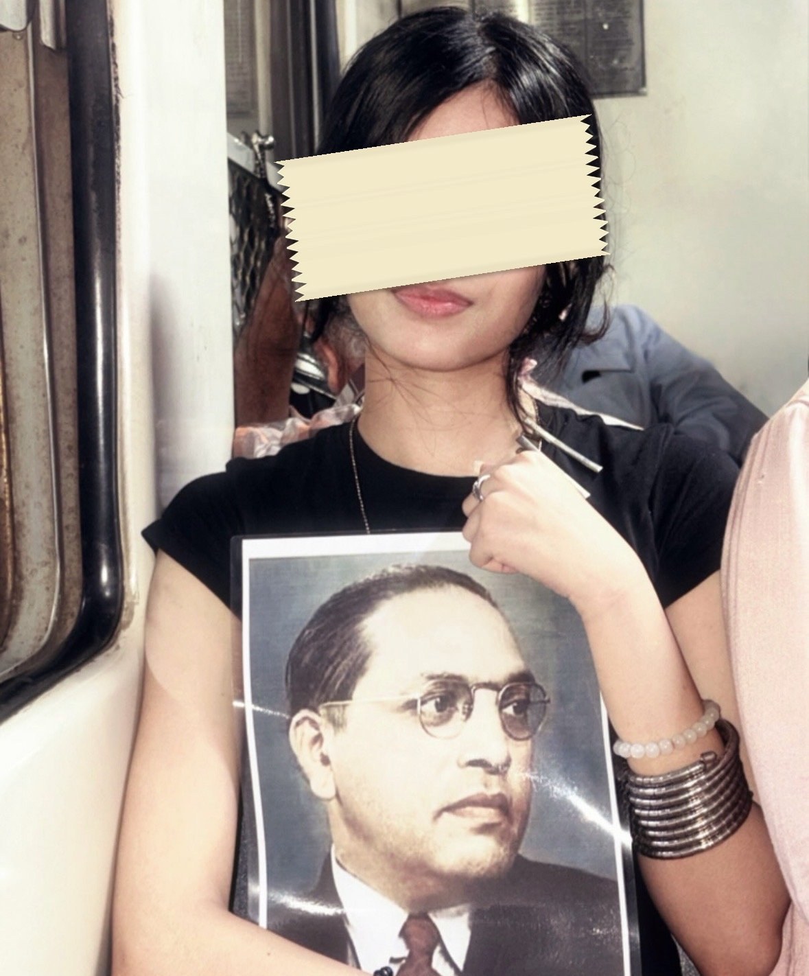 A young woman standing in a train carriage wearing a T-shirt printed with a large portrait of B.R. Ambedkar