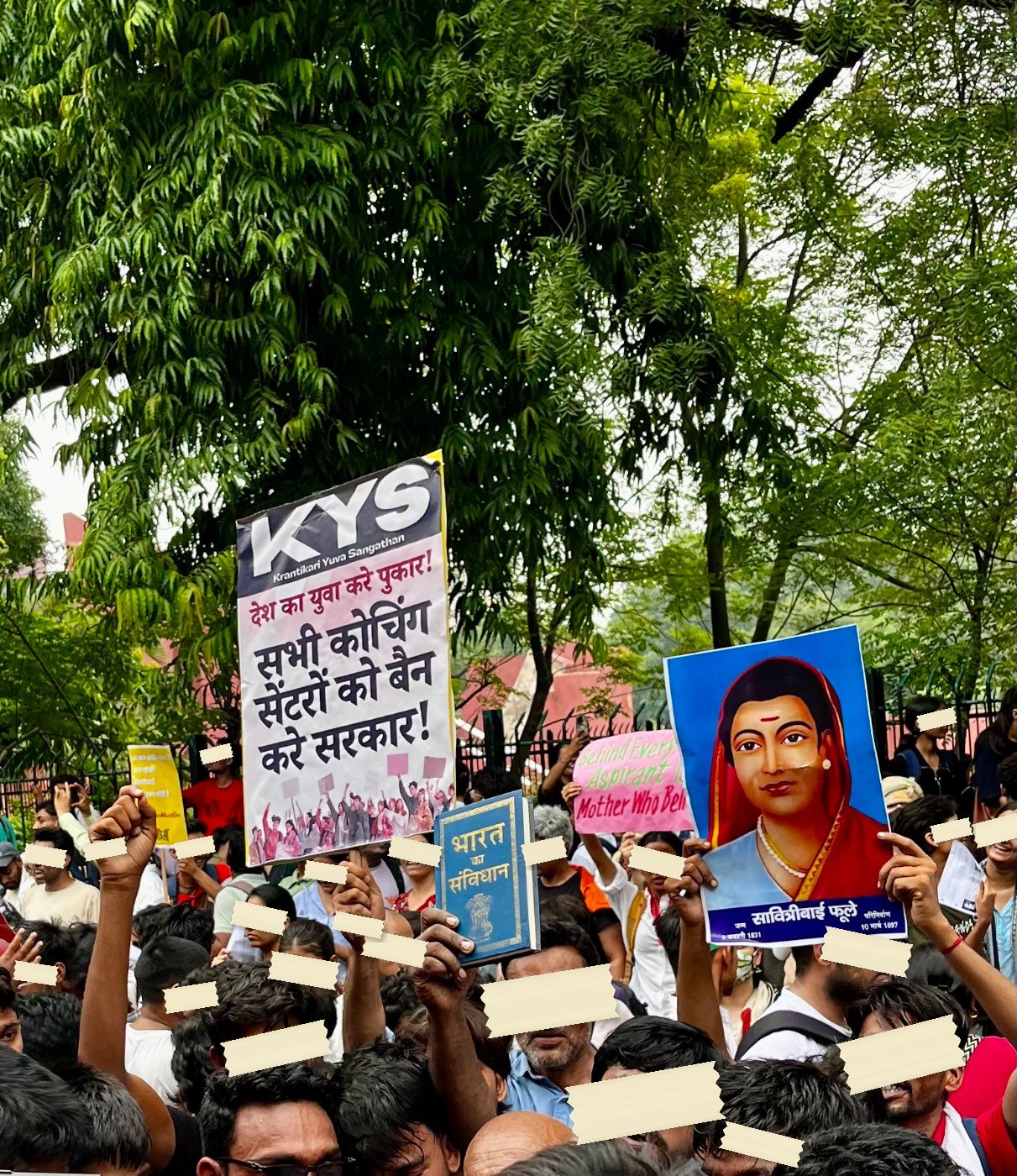 A printed portrait of Savitribai Phule held above a crowd beside a copy of the Constitution