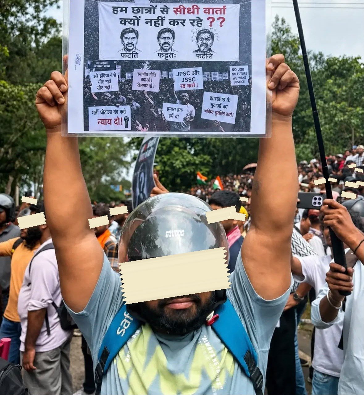 A laminated sheet held above a crowd in Ranchi, printed with a photograph of the protest and its own placards