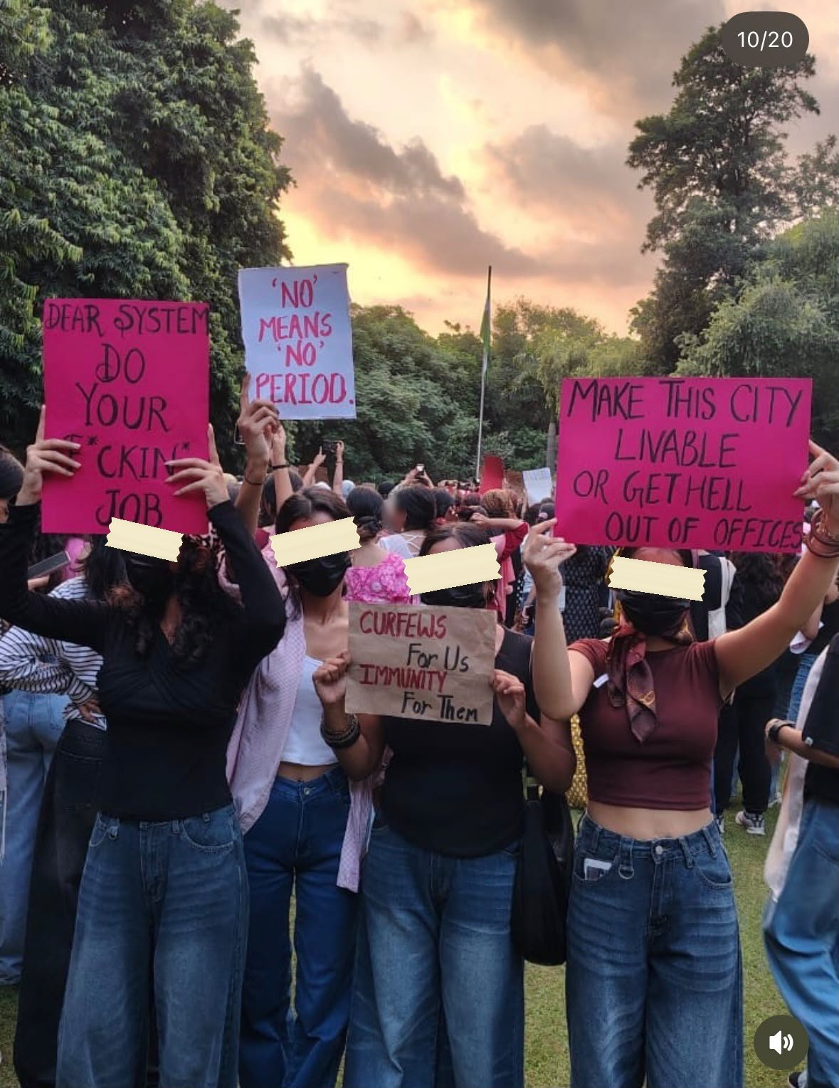 Four women holding pink and cardboard placards at a street march at dusk: DEAR SYSTEM DO YOUR F*CKING JOB, 'NO' MEANS 'NO' PERIOD, CURFEWS For Us IMMUNITY For Them, and MAKE THIS CITY LIVABLE OR GET HELL OUT OF OFFICES.