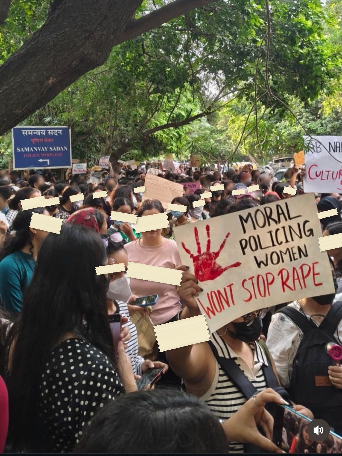 A hand-lettered placard held above a dense crowd on a Delhi street, a red painted handprint beside the words MORAL POLICING WOMEN WONT STOP RAPE.