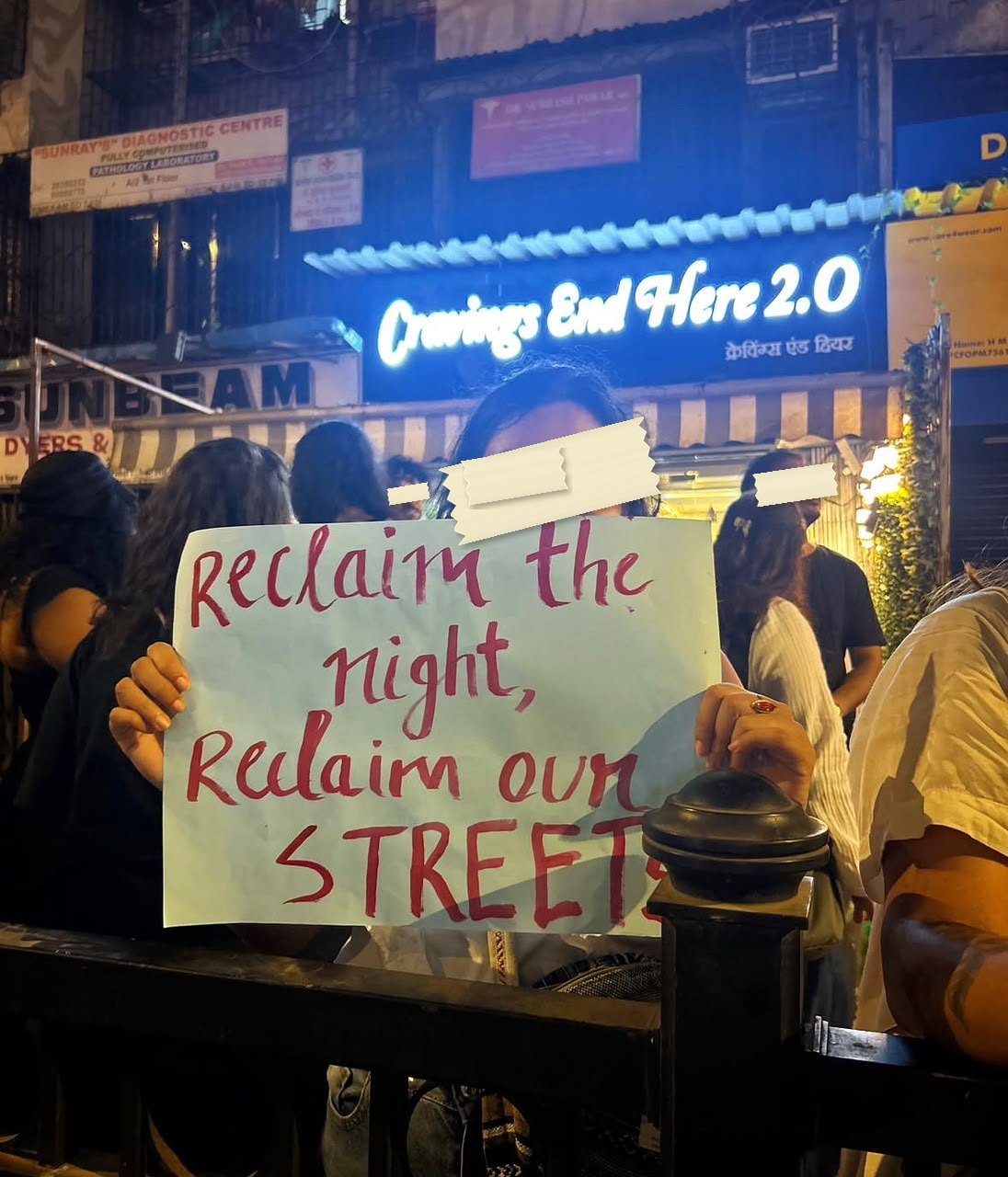 A placard reading Reclaim the night, Reclaim our streets held up at a night march, lit by the neon of a shopfront behind it.