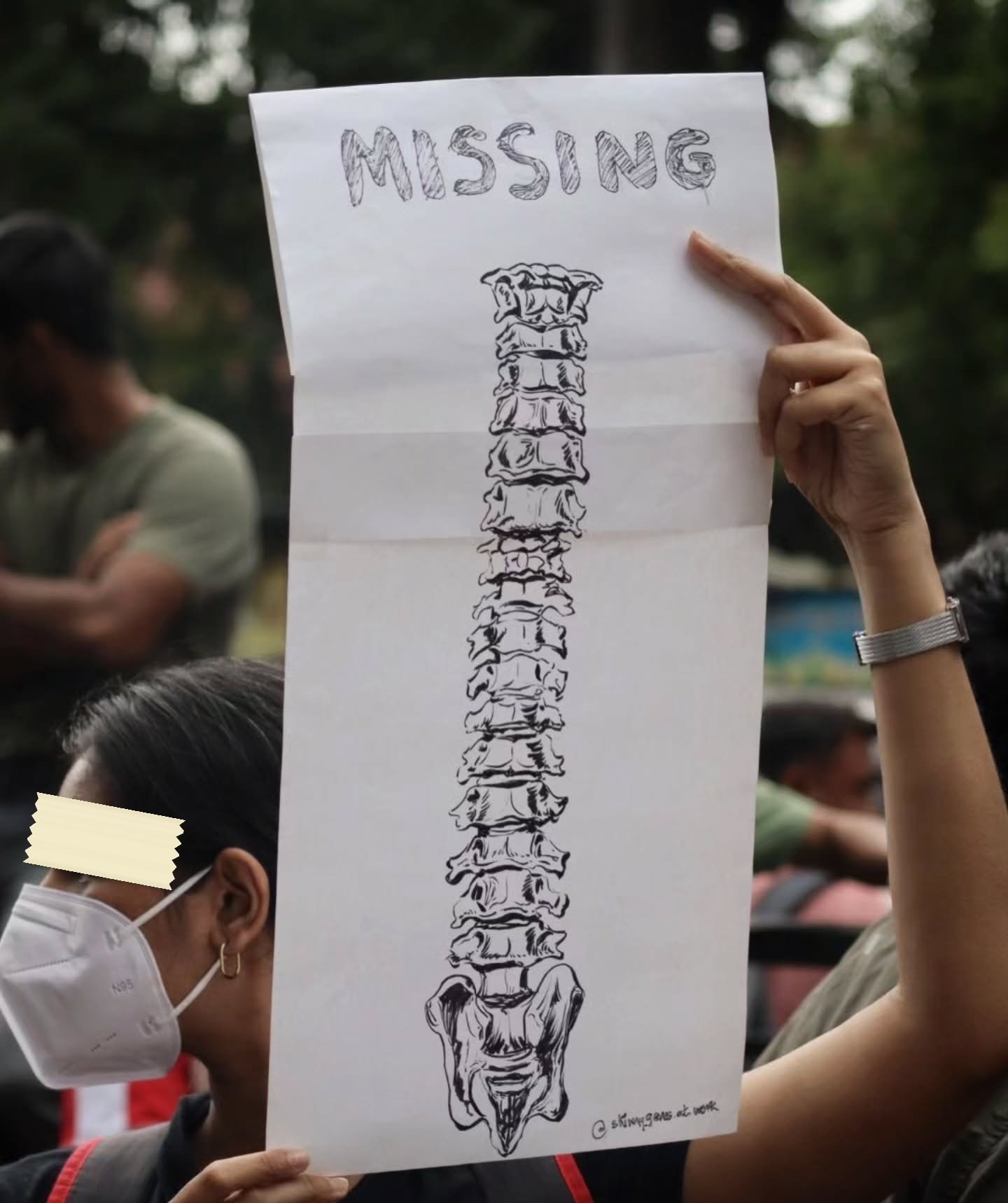A folded white sheet held above a crowd, headed MISSING in outlined capitals, with a careful ink drawing of a human vertebral column below it