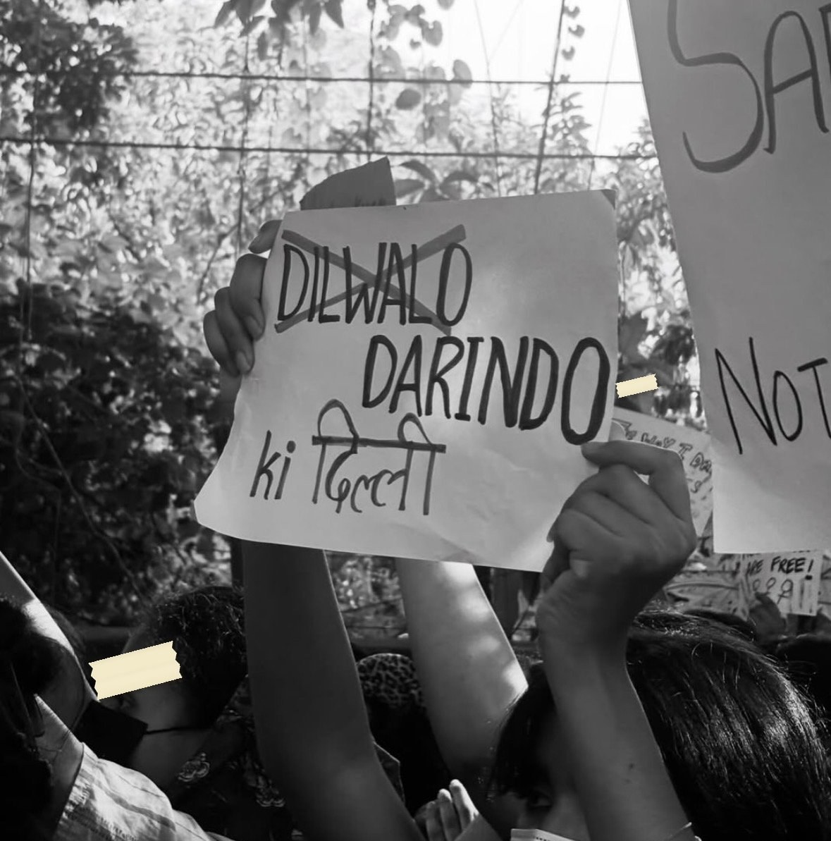 The same edit held up in a crowd and photographed in black and white: DILWALO struck through, DARINDO ki Dilli beneath.