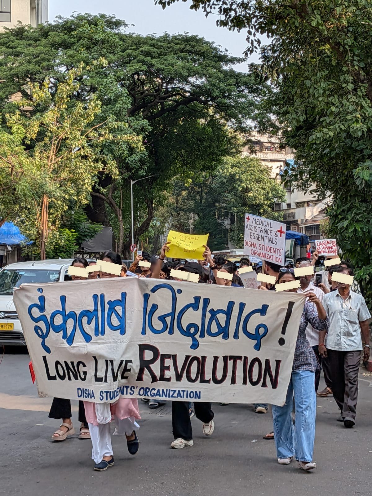 A march in Mumbai behind a long cloth banner reading Inquilab Zindabad in Devanagari and LONG LIVE REVOLUTION beneath it.