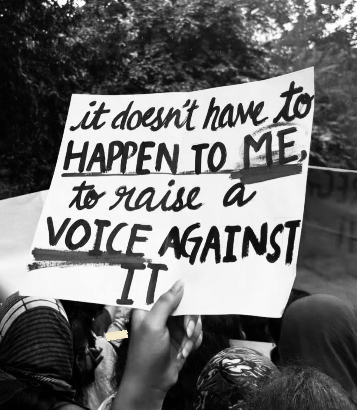 A hand-lettered placard: it doesn't have to HAPPEN TO ME, to raise a VOICE AGAINST IT, with words underlined in heavy marker.