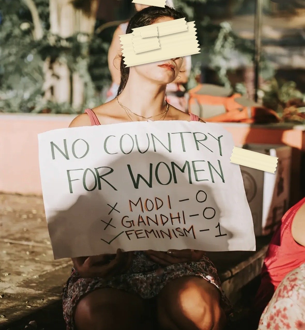 A placard reading NO COUNTRY FOR WOMEN, with a scoreline beneath it: Modi nil, Gandhi nil, Feminism one.